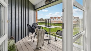 A covered outdoor area with a table and chairs, a view of houses in the background, and a clear sky. - Gorgeous apartment in Fanø with WiFi (Fanø)