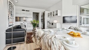A modern kitchen with white cabinetry, a dining area with a round table, and a living room with a black sofa. - Gorgeous apartment in Fanø with WiFi (Fanø)