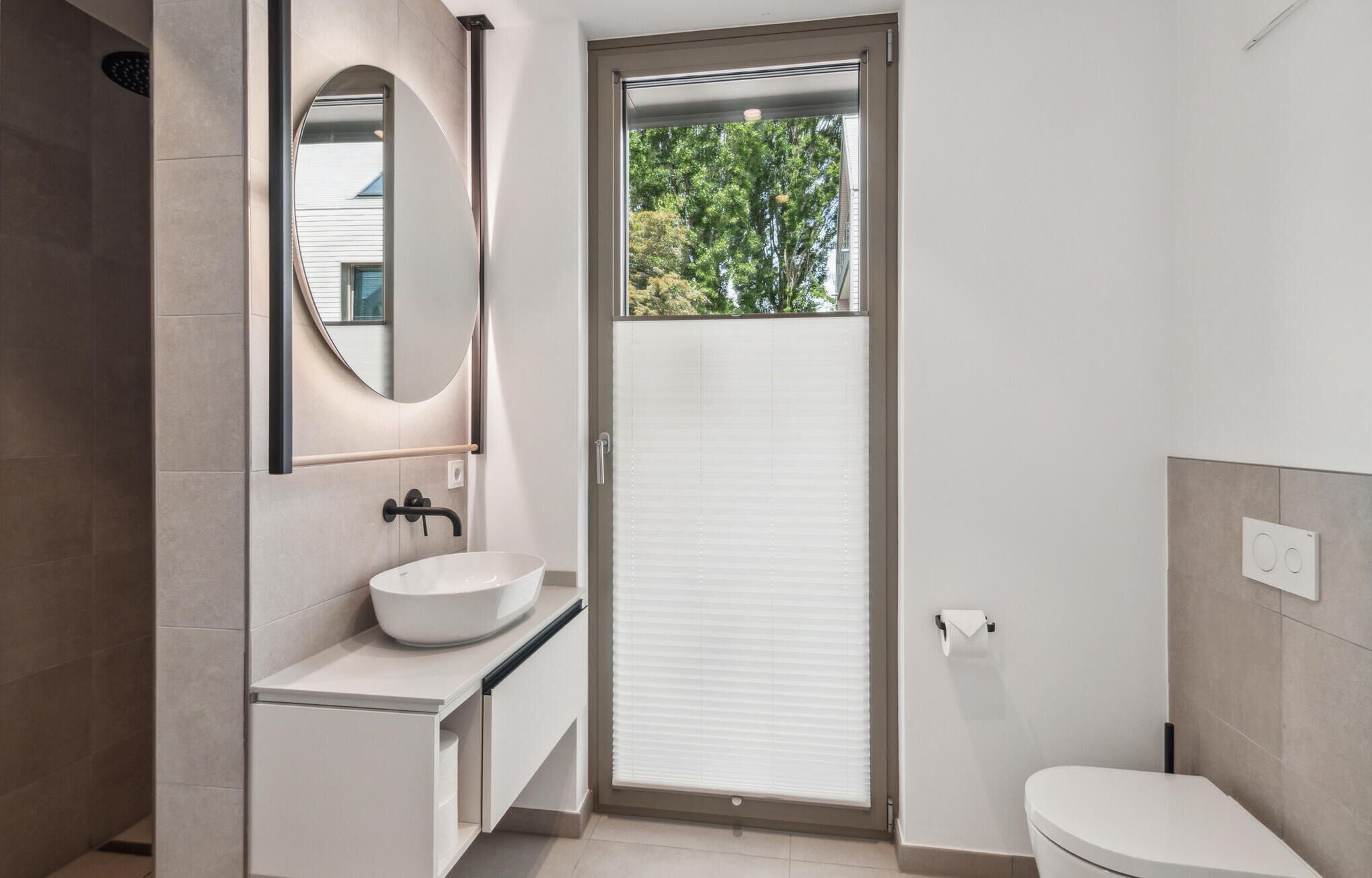A modern bathroom with a white sink, a large mirror, and a toilet.