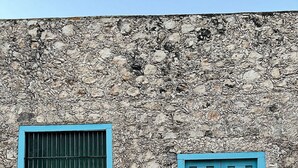 Fachada de edifício com parede de pedra texturizada e duas portas azuis.