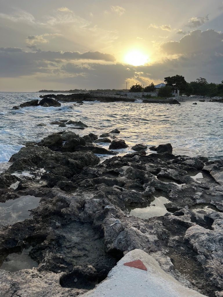 A rocky shoreline with the sun setting in the background.