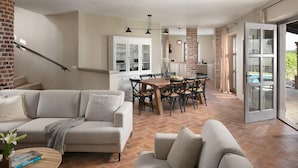 A spacious living area with a sofa, a dining table with chairs, and a kitchen area with cabinets and a brick wall. - 4 bedroom nice home in Sveti Lovrec (Sveti Lovrec)