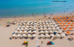 Een strand met rijen parasols en ligbedden, een bewakingspost en een speeltuin.