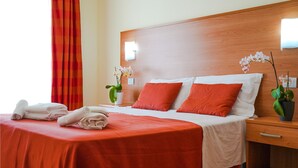 A hotel room with a wooden headboard, a bed with red bedding, two pillows, a nightstand with a lamp, a potted orchid, and a red curtain. - Lovely apartment in Roseto degli Abruzzi (Roseto degli Abruzzi)