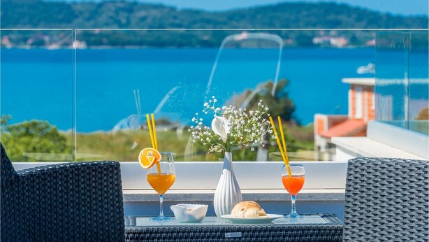 Uma varanda com móveis de vime, um vaso de flores e dois copos de suco de laranja com canudos.