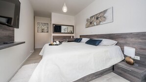 Quarto moderno com uma cama grande, uma TV fixada na parede e obras de arte nas paredes.