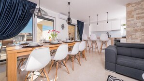 Uma área de jantar moderna com mesa de madeira, cadeiras brancas e vista para o exterior.