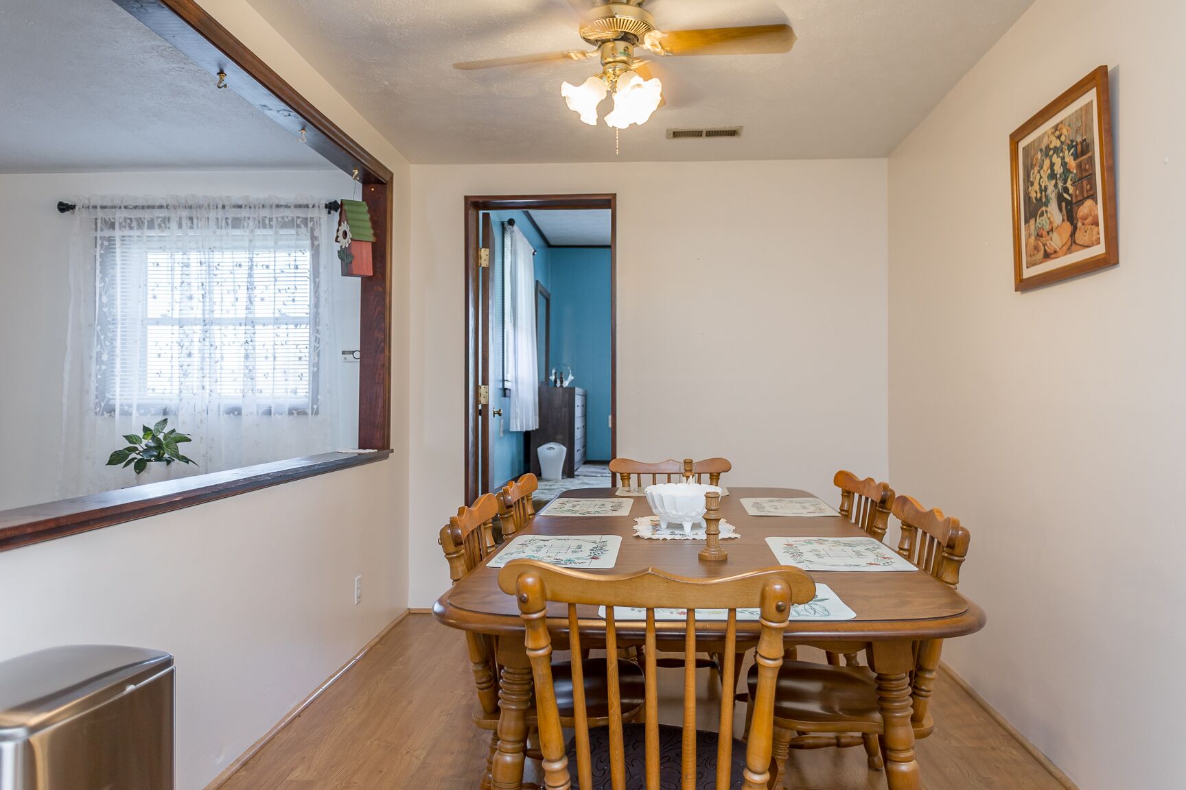 A dining room with a wooden table and chairs, a ceiling fan, and a window with curtains.