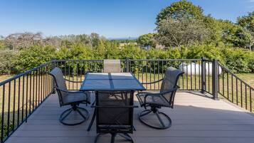 Eine Terrasse mit Tisch und vier Stühlen, umgeben von einem Metallgeländer, mit Blick auf einen angelegten Garten und weit entfernte Hügel.