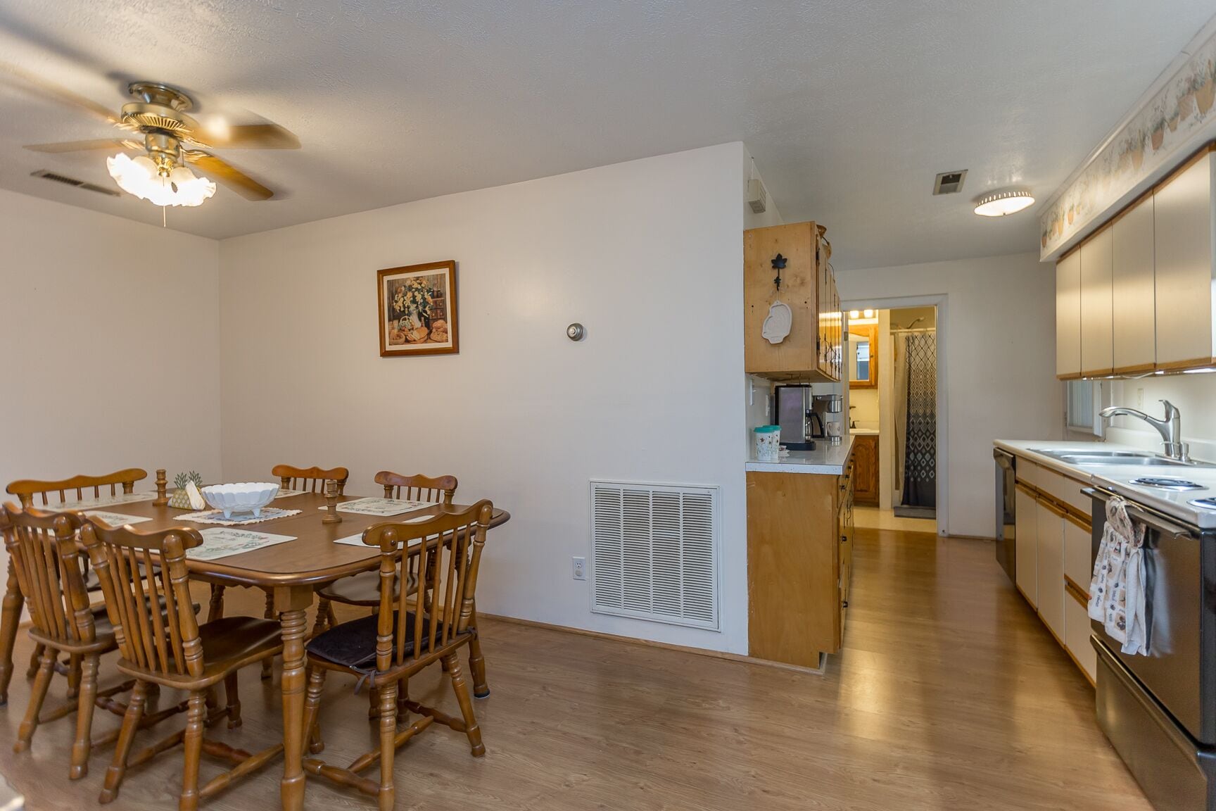 A dining area with a wooden table and chairs, a ceiling fan, and a kitchen with cabinets and a sink.