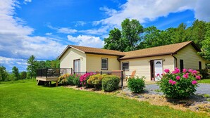 A two-story house with a porch, surrounded by a well-maintained lawn and flowering bushes. - Quiet, off the grid getaway with access to hiking, fishing and wineries nearby! (Bridgewater)
