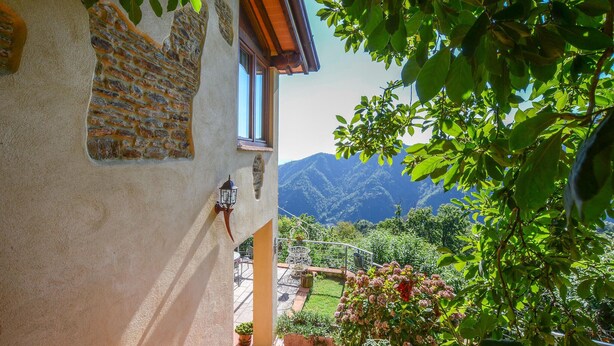 A view from a balcony with a stone wall, a window, and a mountain backdrop.