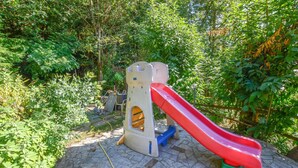 A playground with a slide and climbing structure, surrounded by greenery.