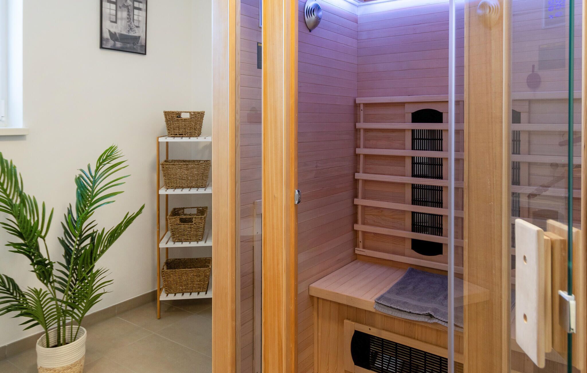 Eine Ecke des Raumes mit einem Holzregal, das Körbe, eine Topfpflanze und eine Sauna mit einem Handtuch auf dem Boden beherbergt.