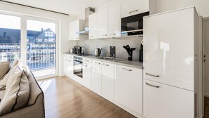 Uma cozinha moderna com armários brancos, forno embutido e uma geladeira grande.