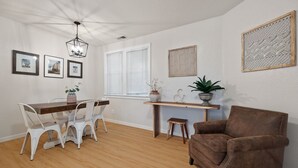 A dining area with a wooden table and white chairs, a brown armchair, and a potted plant. - 2BR Downtown Sac - In unit Laundry - Free Parking (Sacramento)