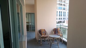A balcony with two wicker chairs and a small table, a glass door leading to a room, and a view of a building in the background. - San Stefano Grand Plaza (Alexandria)