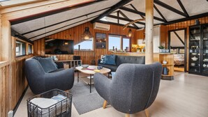 Un interior acogedor y moderno con techo alto y paneles de madera, que presenta un área de descanso con sillones y una mesa de comedor.