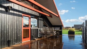 Una terraza de madera con una puerta roja y un espacio cubierto con sillas.