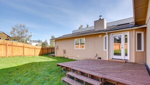 En bostadsträdgård med en träaltan, ett trästaket och ett hus med en skorsten.