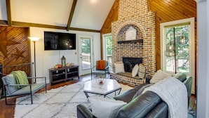 Una sala de estar acogedora con chimenea de ladrillo, televisor de pantalla plana en la pared y un área de estar confortable con sofá y sillones.