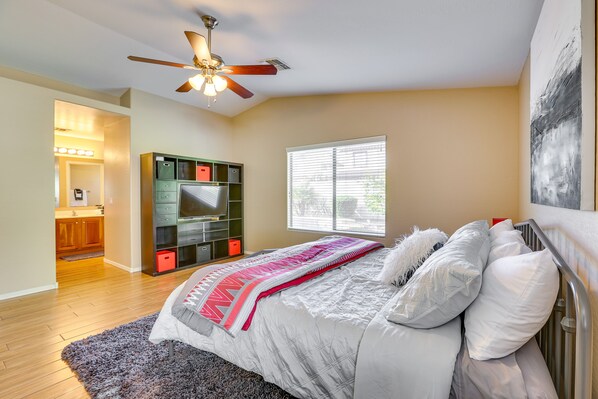 A bedroom with a bed, a ceiling fan, a window, and a built-in TV shelf.