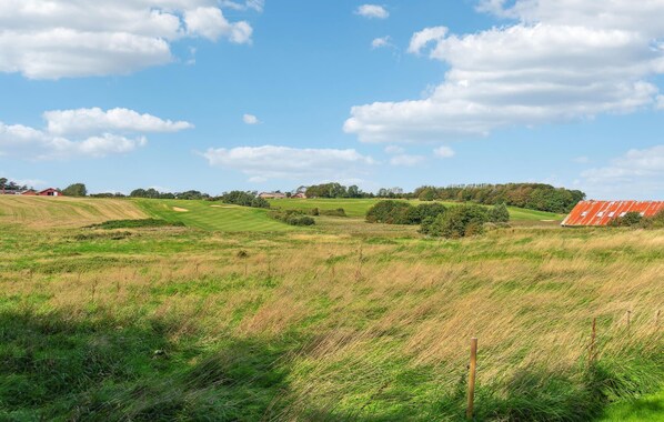 Un paysage rural caractérisé par des collines douces, un ciel dégagé et des bâtiments dispersés.