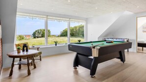Una habitación amplia con mesa de billar, mesa de futbolín y un ventanal con vistas a un campo cubierto de césped.