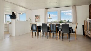 Un comedor moderno con una mesa y sillas de madera, una cocina al fondo y un ventanal con vistas.