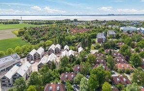 Un área residencial con casas, un edificio grande de techo plano y una masa de agua al fondo.