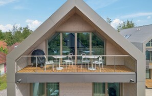Una casa moderna con un balcón grande, ventanas amplias y una terraza de madera.