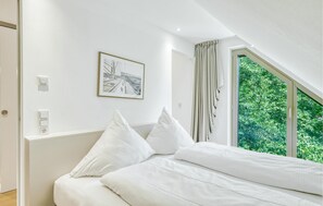 Een slaapkamer met een bed, een raam met gordijnen, een lichtschakelaar aan de muur en een lijst met een afbeelding.