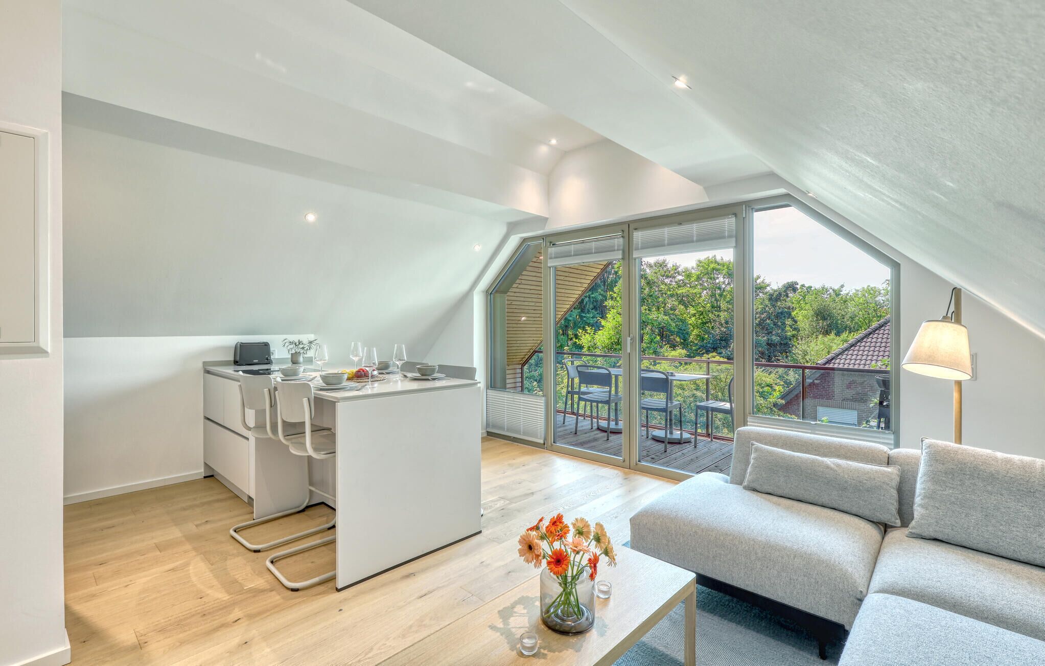 En moderne loftslejlighed med et køkken, spiseplads og en balkon med udsigt over grønne områder.