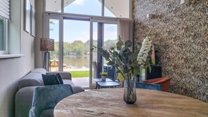 A modern living room with a round wooden table, a sofa, and a view of a lake through large glass doors. - Lovely home in Oosterwolde with WiFi (Oosterwolde)