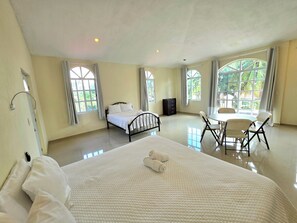 A hotel room with a bed, a small table with chairs, large windows, and a ceiling light.