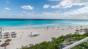 A beach with clear turquoise water, white sand, and a few umbrellas and beach huts. - State of the arts family unit best location beach & pool (CancÃºn)