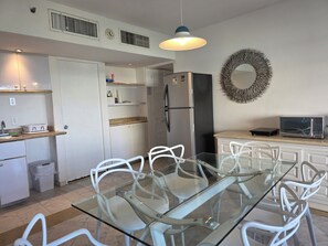 Eine moderne Küche mit einem Glastisch, weißen Stühlen, einem Kühlschrank, einer Mikrowelle und einem dekorativen Kranz an der Wand.
