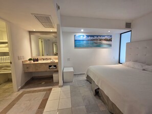 Ein modernes Schlafzimmer mit einem großen Bett, ein Badezimmer mit Waschtisch und ein Bild mit einer Strandansicht.