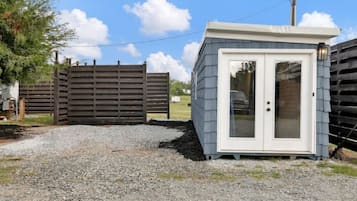 A small, single-story structure with a light blue exterior and a white door, situated on a gravel surface.