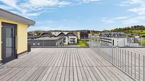 Eine Dachterrasse mit Blick auf Wohnhäuser, ein Holzboden und ein Metallgeländer.