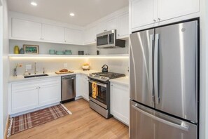 A modern kitchen with white cabinets, stainless steel appliances, and a wooden floor.