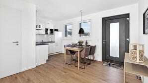 A modern kitchen with white cabinets, a dining table with chairs, and a dark door. - Awesome apartment in Winterberg with sauna (Winterberg)