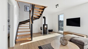 A modern living room with a wooden staircase, a black fireplace, a flat-screen TV, and a sofa. - Awesome apartment in Winterberg with sauna (Winterberg)