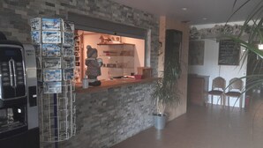 Un'area di accoglienza con parete in pietra, una macchina del caffè KREA e NECTA, una statua e una pianta in vaso.