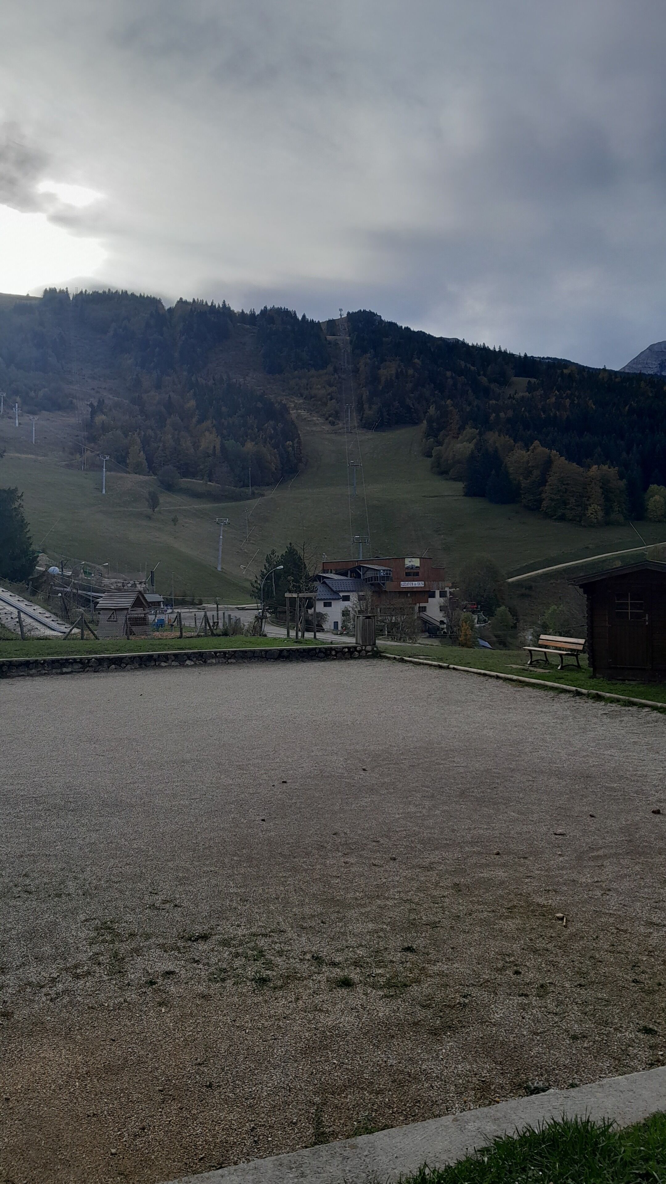 A rural landscape with a gravel area, a wooden bench, and a small building.