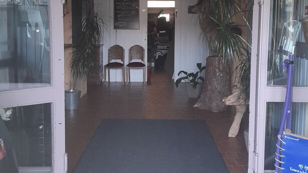 L'ingresso del Le Galax E con un cartello di legno, due sedie all'esterno e un tappetino nero.