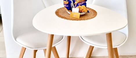 A round white table with two white chairs, a woven placemat, and snacks.