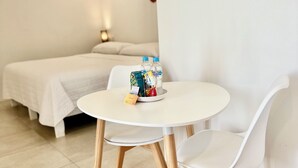 Ein schlicht eingerichteter Raum mit einem runden weißen Tisch, zwei weißen Stühlen, einem Bett mit weißer Bettwäsche und einer Wand mit Dekorationselementen.