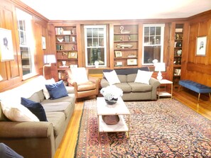 A cozy living room with wooden paneled walls, a brown leather armchair, a beige sofa, and a patterned rug. - Historic Rectory Retreat in Stockbridge – Getaway for 8-12 Guests (Stockbridge)