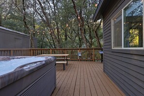 Um deck de madeira com hidromassagem, mesa de piquenique e luzes de cordão.